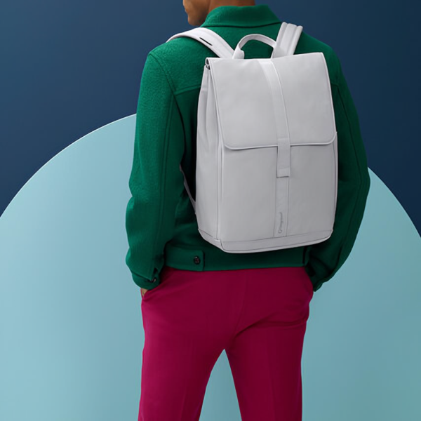 Eine Person trägt einen weißen Bugaboo Wickelrucksack auf dem Rücken, kombiniert mit einer grünen Jacke und pinker Hose vor farbigem Hintergrund.