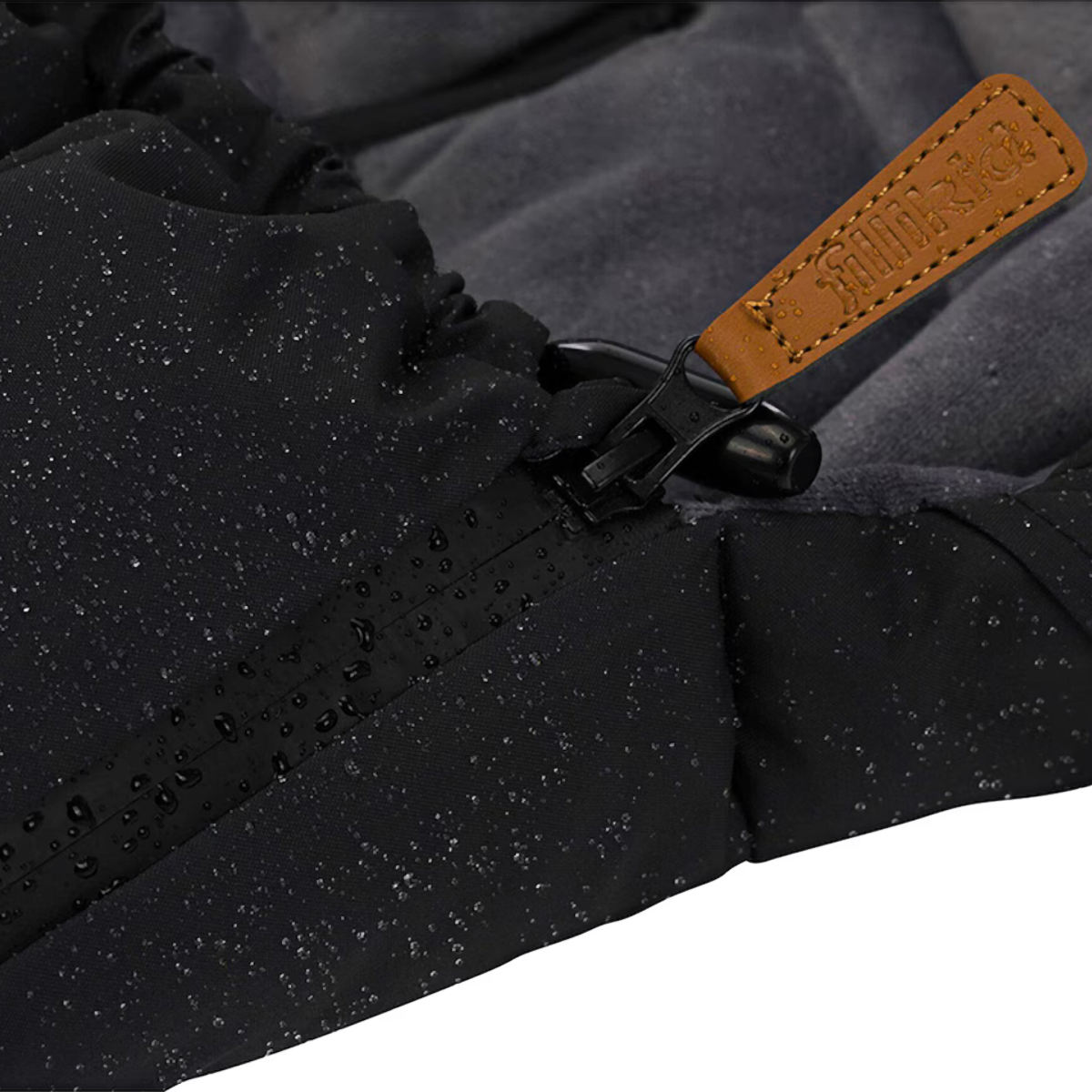 Detailaufnahme eines schwarzen Fußsacks mit Reißverschluss, auf dem Wassertropfen sichtbar sind. Der Zipper hat einen braunen Lederanhänger mit geprägtem Fillikid Logo