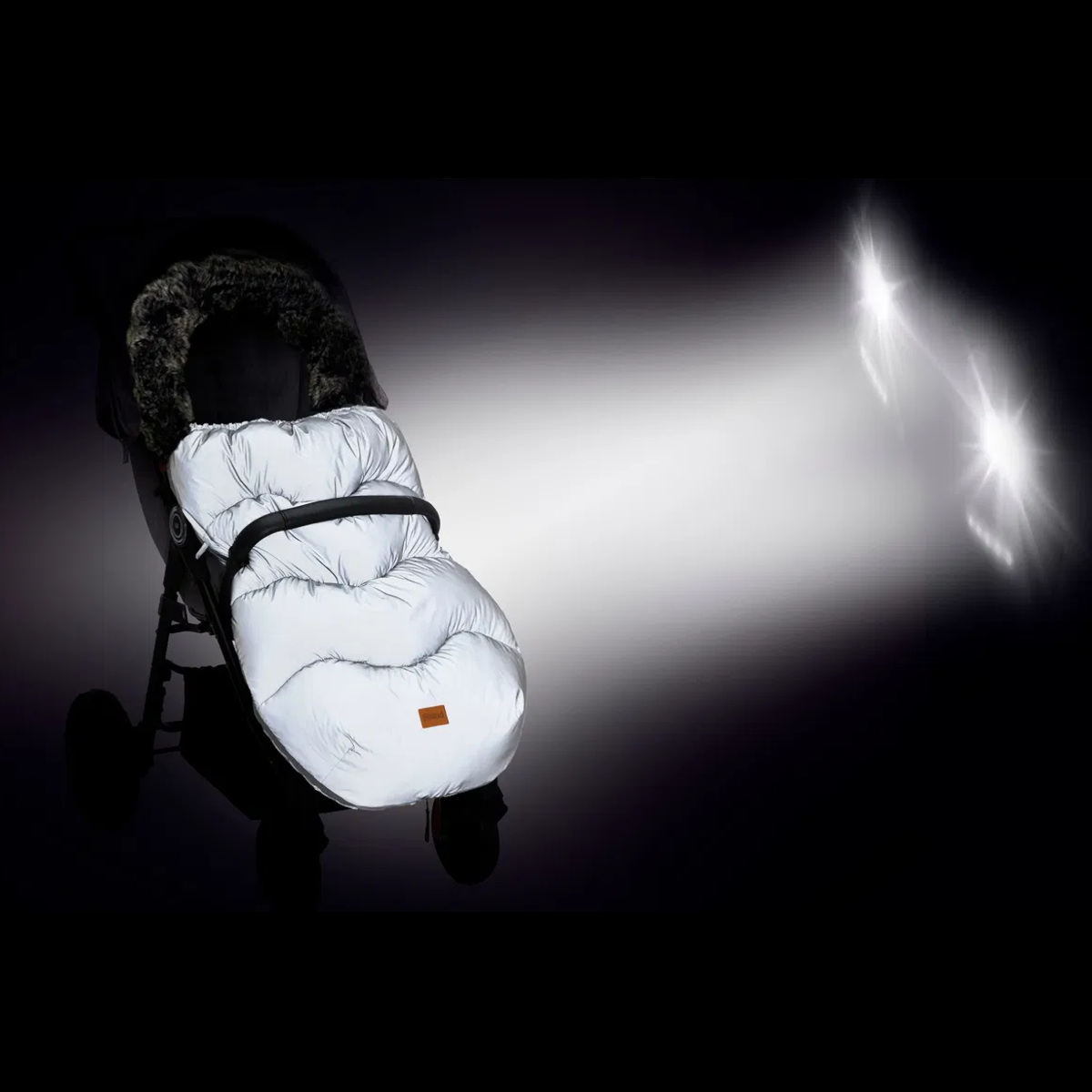 Kinderwagen im Dunkeln mit reflektierendem Winterfußsack. Der Fußsack leuchtet silbrig-weiß im Scheinwerferlicht und ist dadurch deutlich sichtbar.