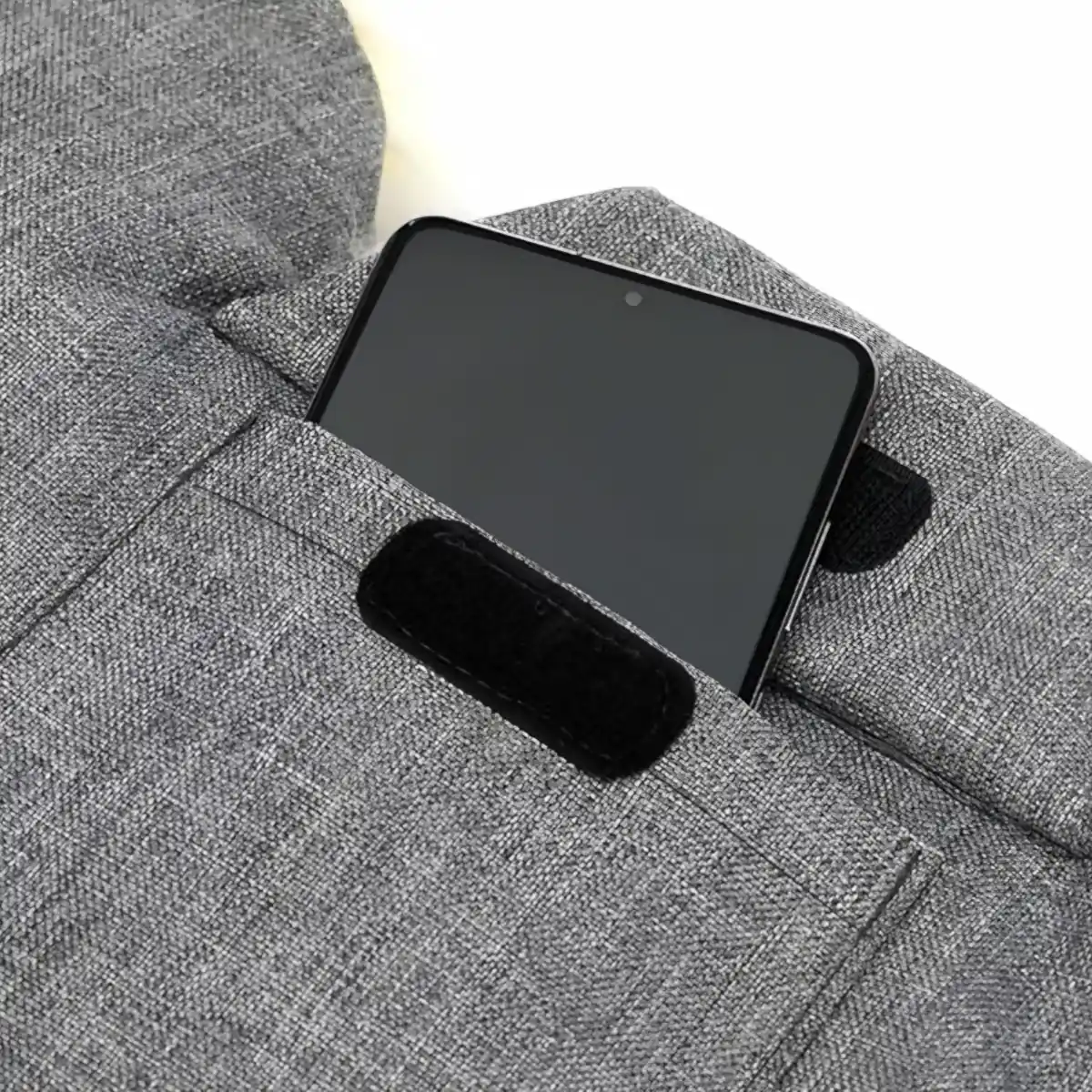 Nahaufnahme einer grauen Stofftasche mit Klettverschluss. Die kleine extra Tasche ist offen und dort steckt ein Smartphone drin. Dieses schaut halb raus.