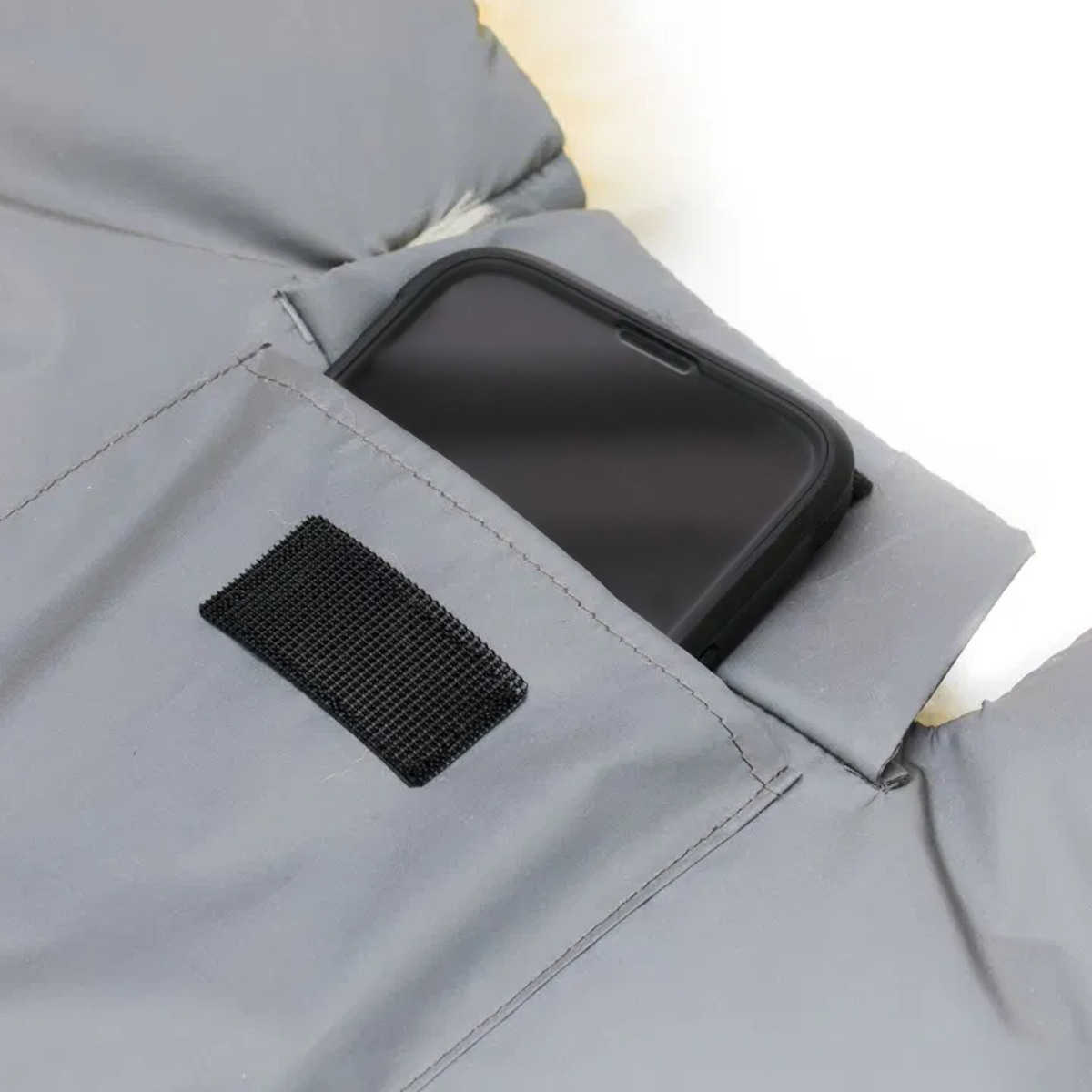 Nahaufnahme einer grauen Stofftasche mit Klettverschluss. Die kleine extra Tasche ist offen und dort steckt ein Smartphone drin. Dieses schaut halb raus.