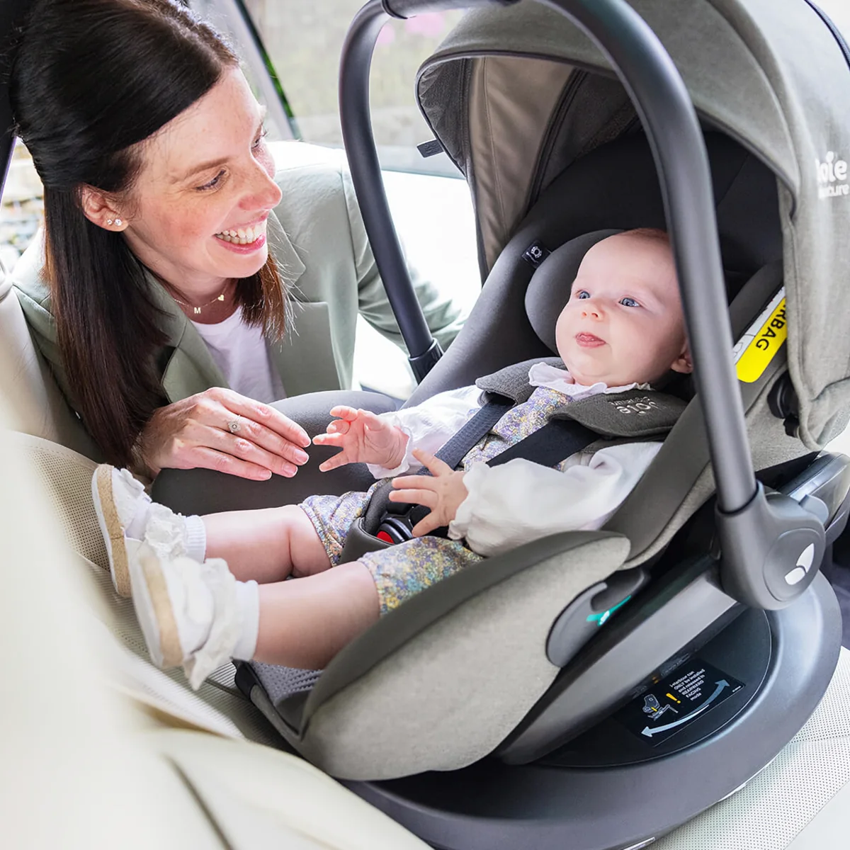 Eine Frau setzt ihr Baby sicher in eine Babyschale im Auto mit i-Size Basisstation.